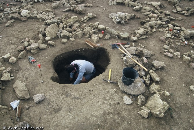 Fouille d'une tombe du VIIIe s. avant notre ère, nécropole de Puisserguier (Hérault), 2003.  Placée au centre d'une construction circulaire en pierre, cette tombe abrite les restes du défunt incinéré, des effets personnels et des vases d'accompagnement. 