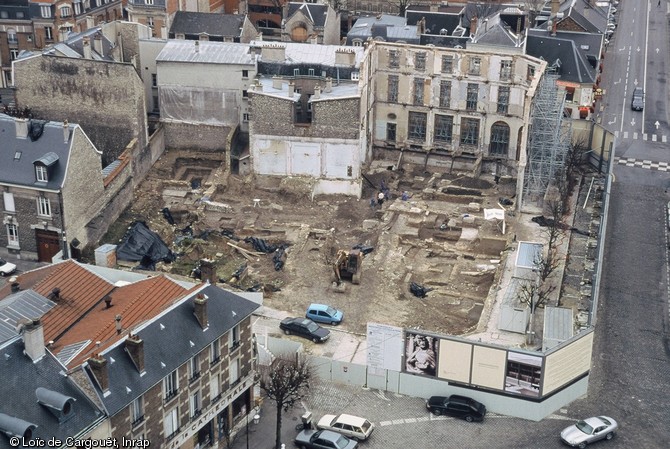 Le chantier archéologique à l'emplacement de la future médiathèque de Reims (Marne) vu depuis la cathédrale, 2000.  La stratigraphie du site est complexe, les vestiges couvrant une période allant du Ier s. avant notre ère jusqu'à l'époque contemporaine. Néanmoins, on peut observer une rue à l'emplacement de la pelle mécanique, séparant deux ensembles où les constructions se sont superposées. 