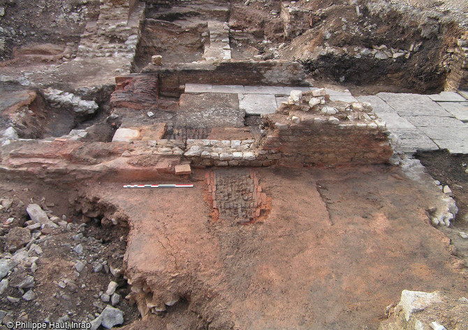 Une partie des thermes publics romains de Besan&ccedil;on (Doubs), fouill&eacute;s en 2005.  Au premier plan, l&rsquo;area (sol en b&eacute;ton de tuileau) constitue la partie inf&eacute;rieure du dispositif de chauffage par le sol (hypocauste). Le foyer, construit en briques, relie la pi&egrave;ce chauff&eacute;e au local de chauffe (o&ugrave; le feu est aliment&eacute;), d&eacute;limit&eacute; par le sol dall&eacute;.