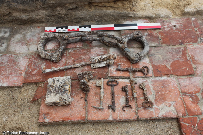 Mobilier trouvé dans les remblais de la destruction de l'un des bâtiments de la prison qui existait au XIXe siècle au pied de logis seigneurial du château médiéval (XIe-XVe siècle) d'Argentan (Orne), 2016. Il s'agit d'une entrave de pied de prisonnier, d'une tirette de porte, d'un bloc de serrure, de plusieurs clés et d'une poignée de porte. 