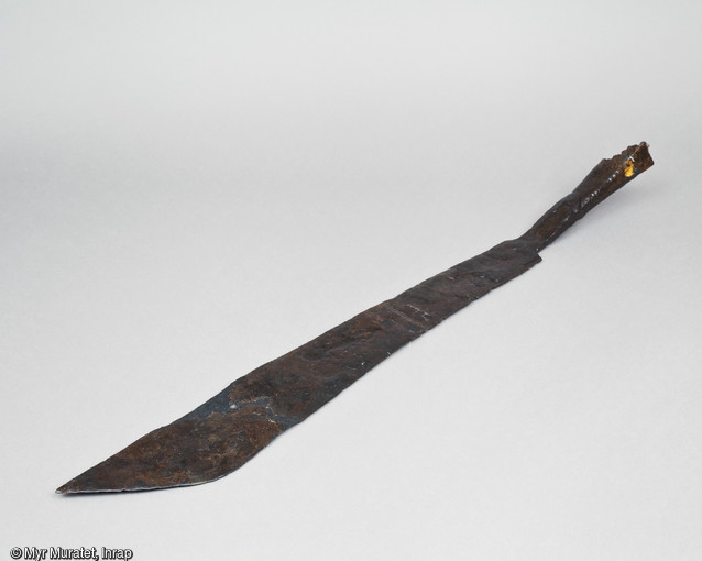 Fauchard en fer, appelée également faux de guerre, 1ère moitié du XVe siècle, longueur : 97 cm, provenant du site de l'Îlot de la Charpenterie à Orléans (Loiret). Utilisée pour le combat rapproché, pour donner des coups de taille et d'estoc, elles permettait notamment de couper les jarrets des chevaux. 