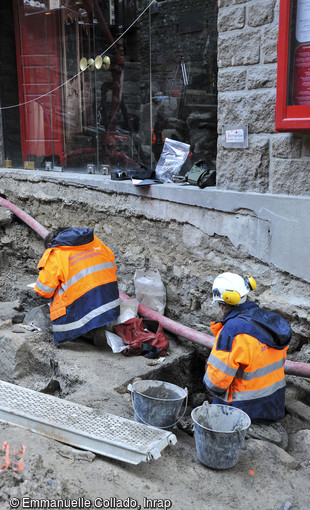 Fouille de s&eacute;pultures et du niveau d'abandon ant&eacute;rieur au cimeti&egrave;re m&eacute;di&eacute;val mis au jour au Mont-Saint-Michel (Manche), 2017. La fouille est contrainte par les nombreux r&eacute;seaux et l'&eacute;troitesse de la rue. 