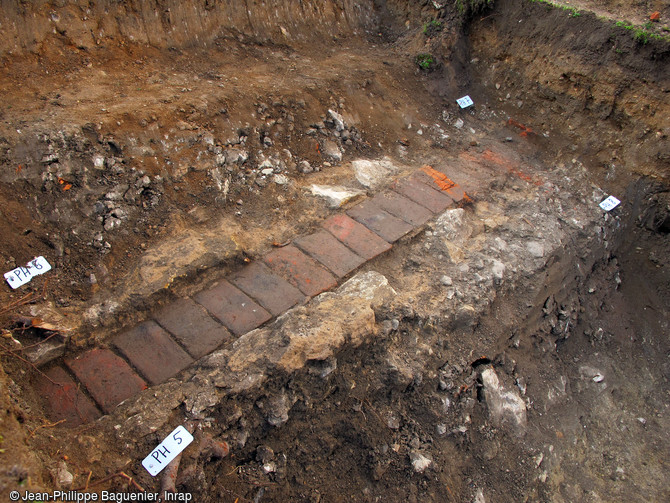 La canalisation en brique au premier plan est un des am&eacute;nagements des jardins du ch&acirc;teau moderne de Buzan&ccedil;ais (Indre). Les vestiges dans la coupe stratigraphique correspondent aux occupations m&eacute;di&eacute;vales et aux plantations des jardins. 
