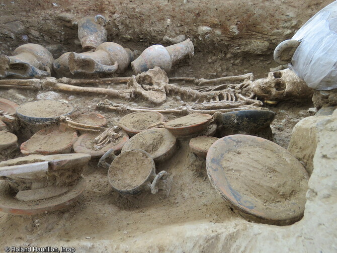 Vue de la chambre funéraire étrusque (IVe siècle av. notre ère) à Aléria (Haute-Corse) depuis le couloir. Au premier plan différentes coupes et coupelles présentant des restes archéozoologiques en cours d'étude. Au second plan, la défunte, au-dessus de sa tête est placé un skyphos consolidé avant dégagement. 