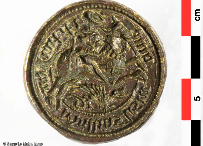 Matrice de sceau avec au centre grav&eacute; en creux un cavalier (saint Georges) surplombant un dragon, entour&eacute; d&rsquo;une l&eacute;gende en lettres gothiques, puis d&rsquo;un cercle perl&eacute;, d&eacute;couvert dans dans&nbsp;une poche de charbons dans l&rsquo;aile nord du logis royal de Villers-Cotterets (Aisne), en 2022. La l&eacute;gende peut &ecirc;tre lue : &laquo; I P PRI/EUR / DEVILLERS / LESM / OINE &raquo;.