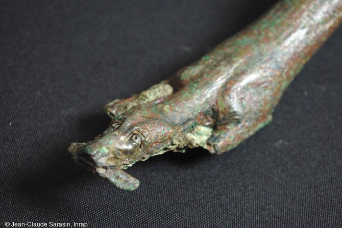 D&eacute;tail de l'anse de l'authepsa d&eacute;couverte lors d'une fouille &agrave; Die (Dr&ocirc;me). Elle repr&eacute;sente un chien allong&eacute;, les oreilles en arri&egrave;re, les yeux repr&eacute;sent&eacute;s par deux billes d'argent. Il tient une proie non identifiable dans sa gueule. R&eacute;alis&eacute;e avec la technique de la cire perdue, cette anse pr&eacute;sente des d&eacute;tails anatomiques remarquables, comme le retroussement des babines, des sourcils et du contour des yeux. 