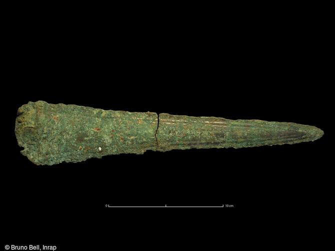Poignard en bronze retrouv&eacute; dans la tombe princi&egrave;re &agrave; Giberville (Calvados) en 2020. Il date de l'&acirc;ge du Bronze ancien (vers 1800-1600 ans avant notre &egrave;re), avec ses rivets de fixation en haut de la lame. De type armoricain (sous-type Longues ou Bourbiac), il pr&eacute;sente un d&eacute;cor de deux filets parall&egrave;les sur les tranchants. Ce type d 'arme retrouv&eacute; dans les tombes avec des pointes de fl&egrave;ches est &eacute;galement r&eacute;v&eacute;lateur des &eacute;lites sociales de cette &eacute;poque. 