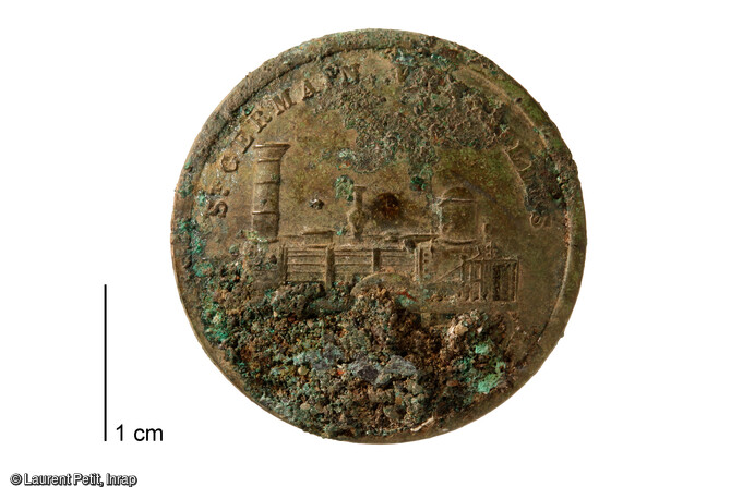 Bouton en m&eacute;tal d'un habit d'employ&eacute; de la gare mis au jour lors de la fouille de l'ancienne gare du Pecq (Yvelines) en 2017. Il est orn&eacute; d'un d&eacute;cor en bas relief d'une locomotive. On lit l'inscription Saint-Germain Versailles, du nom de l'une des compagnies fond&eacute;es en 1837 par les fr&egrave;res P&eacute;reire. 