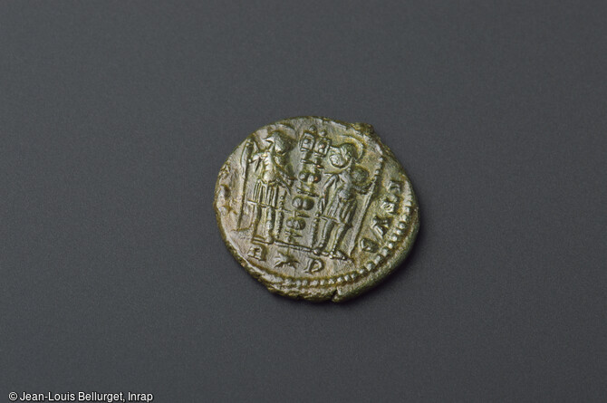 Revers d'une monnaie en bronze, frapp&eacute;e en 335-336, repr&eacute;sentant&nbsp; deux soldats arm&eacute;s et casqu&eacute;s tenant des enseignes militaires. La face est &agrave; l'effigie de l'empereur Constantin 1er. D&eacute;couverte lors de la fouille de la Zac Pasteur &agrave; Besan&ccedil;on (Doubs) entre 2010 et 2011.