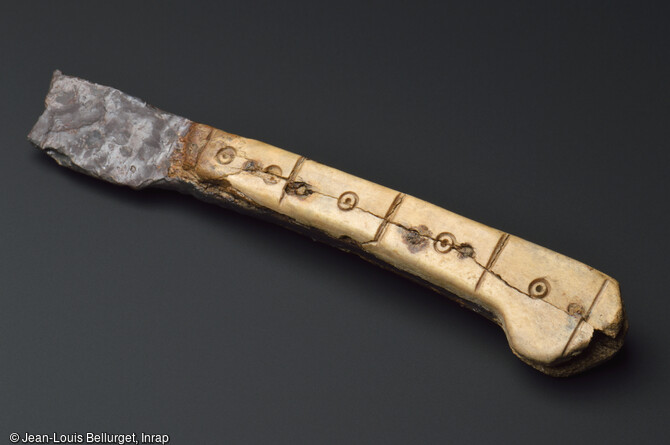 Couteau en fer, 15e si&egrave;cle, d&eacute;couvert lors de la fouille de la Zac Pasteur &agrave; Besan&ccedil;on (Doubs) entre 2010 et 2011. Le manche est constitu&eacute; de deux plaquettes en os d&eacute;cor&eacute;es de petits cercles point&eacute;s, s&eacute;par&eacute;s par de petits traits verticaux. 