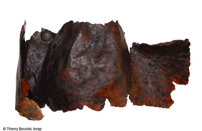 Umbo de bouclier du 1er si&egrave;cle av. notre &egrave;re, dont les ailettes ont &eacute;t&eacute; soulev&eacute;es lors de son arrachement de la planche du bouclier, mis au jour dans un foss&eacute; du sanctuaire gaulois de Saint-Just-en-Chauss&eacute;e (Oise). L'umbo est une pi&egrave;ce qui couvrait le manipule et prot&eacute;geait la main, tout en assurant son renfort. 