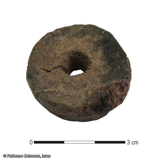 Portion cylindrique de merrain utilisé pour réaliser une fusaïole : la surface perlée a été grossièrement raclée et une perforation circulaire a été aménagée dans le corps spongieux. Dimensions : Diam. : 4,1 cm ; ép. 1,2 cm.  Il est issu d'une cabane dont le mobilier céramique n’a pas permis d’attribution plus précise que le Moyen Âge indéterminé. 