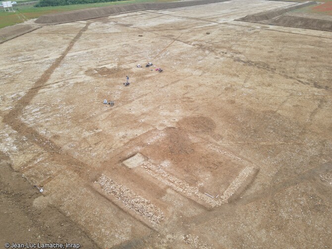 Vue aérienne du bâtiment en pierre situé dans l'enclos d'habitation au premier plan, et fouille des bâtiments sur poteaux au second plan, Ier et IIe siècles à Frénouville (Calvados).