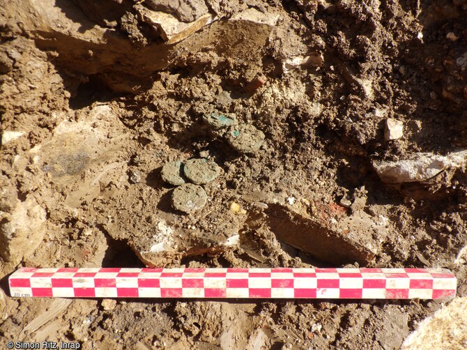 Le dépôt monétaire de l'Antiquité tardive lors de sa découverte dans la cave de la villa de Lemud (Moselle). Ce dépôt est composé d'une vingtaine de monnaies valentiniennes qui illustre les travaux de récupération des matériaux architecturaux de la villa après son abandon, que l'on peut situer grâce à ces monnaies dans la seconde moitié du IVe siècle de notre ère. 