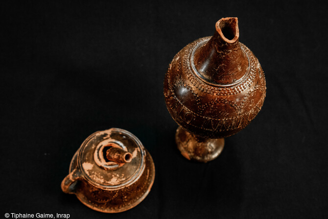 Exemple d'une cruche avec son entonnoir pr&eacute;sentant un manque sur le bord et une cassure de l'embout de l'entonnoir d&eacute;couvert dans une s&eacute;pulture de l'ensemble fun&eacute;raire antique de Saint-Vulbas (Ain). Plusieurs traitements particuliers sont visibles sur les vases, allant &agrave; la d&eacute;coupe du bord &agrave; l'arrachement des cols ou des anses avec plusieurs gestes sur le m&ecirc;me vase. 