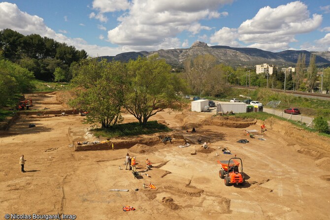 Vue aérienne du site d'Aubagne (Bouches-du-Rhône). L'emprise de la fouille se situe en limite de la plaine alluviale de l'Huveaune, sur le bas du versant de la colline des Passons, en rive gauche de la rivière de la Maïre. Ce site a été recouvert à la fois par des dynamiques colluviales entretenues par l'érosion du versant et par des processus alluviaux nourris des apports de la rivière et de l'Huveaune. Les vestiges archéologiques les plus anciens sont ainsi apparus à une profondeur d'1,10 m sur le versant et à plus de 2,40 m dans la partie septentrionale en contact avec l'ancienne terrasse a