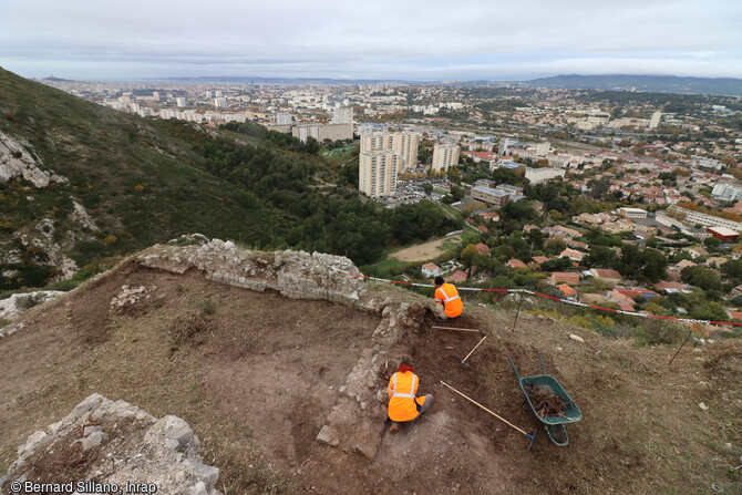 Mise au jour du mur 35 au cours de la fouille du château Saint-Marcel à Marseille (Bouches-du-Rhône). Au fond Marseille et la baie. Ce mur de refend sépare deux espaces : à gauche, probablement un bâtiment à plusieurs étages et à droite une cour. 