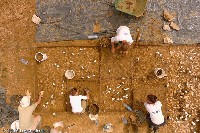 Fouille en carroyage du secteur préhistorique à Arbois (Jura). Suite au décapage, l'équipe a identifié des éléments lithiques taillés, ce qui a conduit à la mise en place de cette fouille en carroyage qui a permis de circonscrire un secteur plus ou moins dense en mobilier. Il s'agit de matériaux siliceux taillés attestant de l'occupation du site au cours de la préhistoire par des groupes de chasseurs-cueilleurs nomades.  