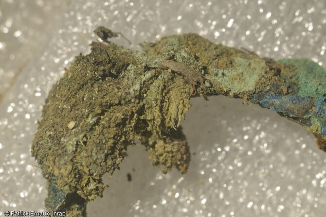 Tissu minéralisé sur une boucle de ceinture du XIIe-XIIIe siècle, provenant d'une inhumation à La Flotte sur l'île de Ré (Charente-Maritime). L'observation du mobilier retrouvé au cours de la fouille tend à rapprocher celui-ci de la culture matérielle des sociétés de la mer du Nord et n'a pas d'équivalent en France ce qui rend les comparaisons difficiles. Les analyses de ces matériaux permettront de connaître leur origine.