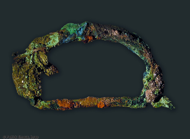 Boucle de ceinture du XIIe-XIIIe siècles, avec tissu conservé sur ses côtés, provenant d'une inhumation à La Flotte sur l'île de Ré (Charente-Maritime). L'observation du mobilier retrouvé au cours de la fouille tend à rapprocher celui-ci de la culture matérielle des sociétés de la mer du Nord et n'a pas d'équivalent en France ce qui rend les comparaisons difficiles. Les analyses de ces matériaux permettront de connaître leur origine.