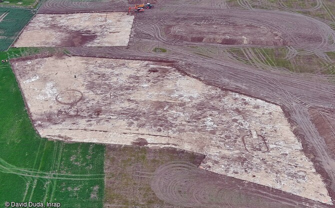 Vue aérienne vers l'ouest du décapage du site de fouille à Plancy-l'Abbaye (Aube). A droite sur la zone au premier plan, enclos sub-rectangulaire aux angles arrondis et ouvert à l'est. A gauche enclos circulaire et enclos en fer à cheval accolé, au fond à gauche petits enclos quadrangulaires. 