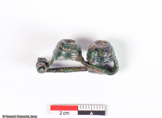 Fibule en alliage cuivreux du type dit  à double timbale  attribuée à la fin du Hallstatt D3-début de la Tène A, découverte dans une inhumation à Plancy-l'Abbaye (Aube).