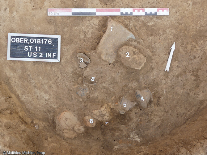 Fond de la fosse 11 datée du Bronze final et tapissée d'artefacts dont un croissant d'argile en terre cuite et un gobelet à col décoré, Oberschaeffolsheim (Bas-Rhin).