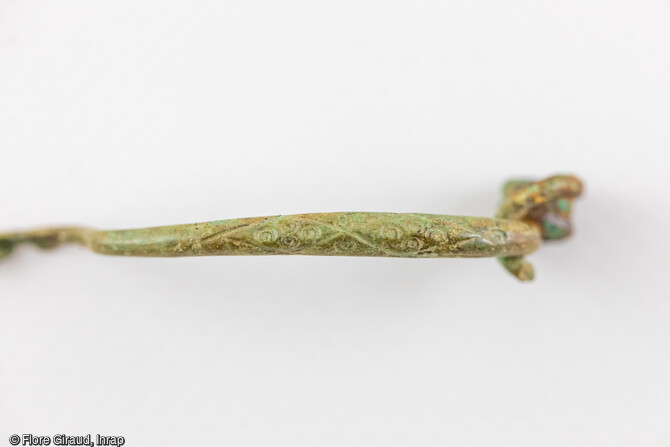 Détail du décor à ocelles et courbes sinueuses incisées sur le dos de l’arc de la fibule en alliage cuivreux découverte dans la sépulture.