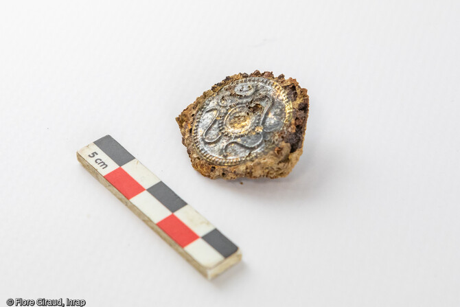 Cabochon de fibule en alliage ferreux, décoré d’un disque serti d’une feuille d’argent au motif repoussé, avec une frise de quatre esses encadrée de grènetis. Pièce d’apparat datée entre la fin du IVe et le début du IIIe s. av. J.-C.