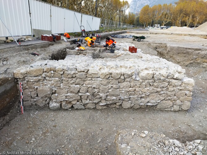 Vue du mur méridional de l'édifice.  Parmi les vestiges mis au jour figure, en limite d’emprise, un édifice quadrangulaire, arasé au niveau des premiers sols de l’Esplanade. La fouille a montré qu’il avait été fondé sur une légère surélévation de la terrasse alluviale, qu’il a été construit d’un seul tenant, sans reprises manifestes, et que son côté oriental était protégé par un fossé drainant. Grâce aux datations effectuées lors du diagnostic, cet édifice était au moins utilisé au début de la Période Moderne – ce qui en fait la première occupation connue de l’emprise fouil