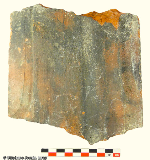 Vue d'une surface d'une tuile sur laquelle a été dessinée une  croix huguenote  (?), l'autre face comportant une inscription  (SAI)NT MARTIN  découverte dans des remblais disposés préalablement à l'installation du sol dallé du temple Saint-Martin de Montbéliard (Doubs). 