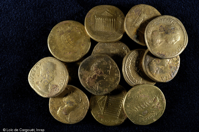 Sesterces en bronze du dépôt monétaire des Mesneux (Marne), 2010.  Enterré au IIIe s. de notre ère, le dépôt est constitué de 336 sesterces et 6 dupondii, pour un poids total de 8 kg. Les pièces ont toutes été frappées au IIe s., à partir du règne d'Hadrien jusqu'au début de celui de Septime Sévère. Au centre de la photo on peut reconnaître à sa légende une pièce frappée sous Commode. 