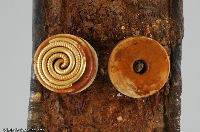 Détail de deux appliques cylindriques ornant le tiers supérieur du fourreau de l'épée découverte dans la sépulture aristocratique n° 11 de Saint-Dizier (Haute-Marne) datée du VIe s. de notre ère, 2002.  L'applique de gauche est en pierre surmontée d'un motif en or enroulé et celle de droite est en ivoire. Ce décor serait issu d'une tradition orientale progressivement arrivée dans les environs de 500 en Europe centrale sous la poussée des Huns. 