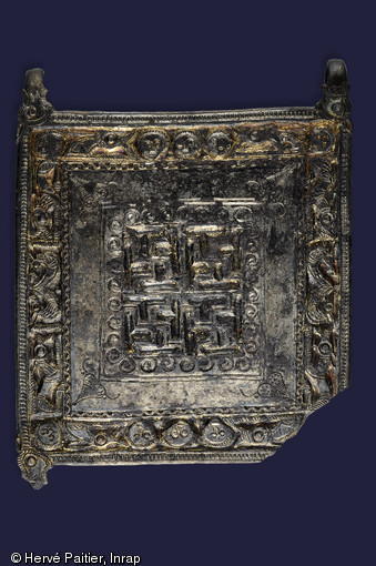 Plaque avec quatre agrafes de fixation grav&eacute;e d'animaux, de svastikas et de visages. Elle ornait le v&ecirc;tement de l'un des d&eacute;funts d&eacute;couvert dans l'une des s&eacute;pultures de la n&eacute;cropole de Saint-Marcel (Morbihan), Ve s. de notre &egrave;re, 2006.