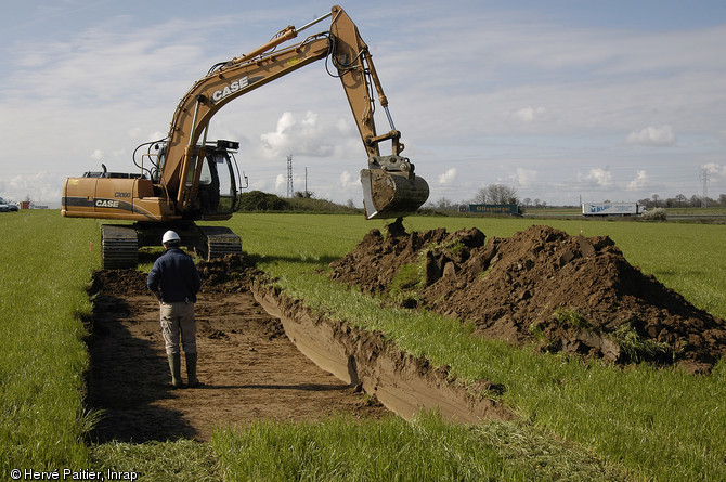 Tranchées de sondages archéologiques réalisées dans le cadre d'un projet d'aménagement à Pacé (Ille-et-Vilaine), 2007.  L'enlèvement de la terre végétale sur 5 à 10 % de la surface concernée permet de localiser la présence de sites archéologiques menacés de destruction.