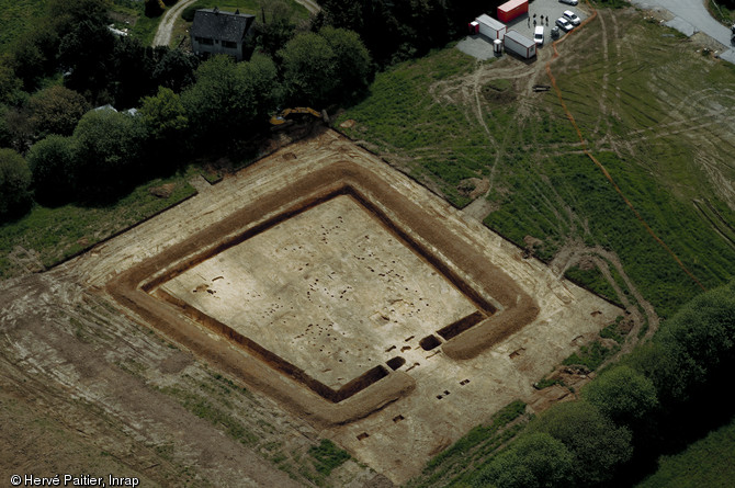 Vue aérienne en fin de fouille de l'habitat gaulois de Corps-Nuds (Ille-et-Vilaine), daté entre la fin de La Tène moyenne et la fin de La Tène finale, 2009.  Un fossé trapézoïdal délimite un espace occupé par neuf bâtiments sur poteaux (habitat et annexes agricoles). L'unique accès à l'espace interne s'effectue par un porche monumental. 