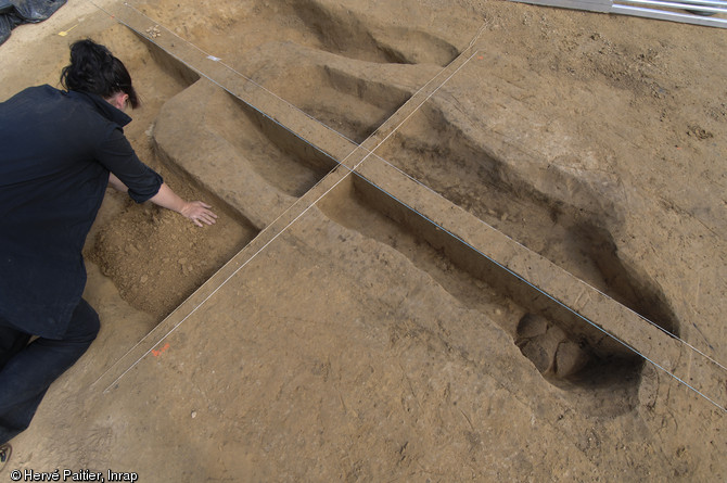 Une archéologue dégage une sépulture en coffre de bois située au centre de l'un des tumulus du site.