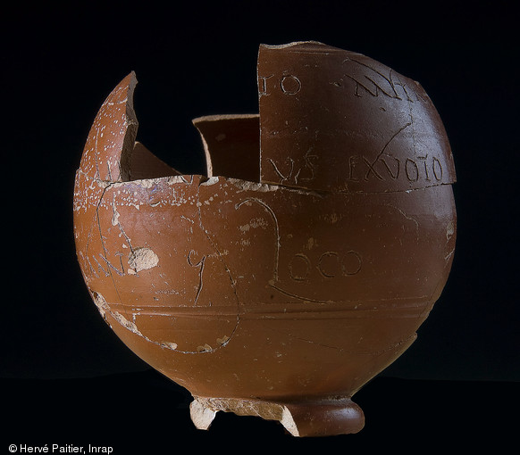 Gobelet sphérique en sigillée rouge foncé (7cm de hauteur) avec inscription gravée avant cuisson à Lezoux, IIe-IIIe s. de notre ère, découvert dans le sanctuaire voué au culte de Mithra à Angers (Maine-et-Loire), 2010.  L'inscription peut être lue : [à l'empereur et] au Dieu invaincu Mithra, []us Genialis, citoyen ambien (?), en raison d'un vœu accompli, a fait don [aux...], à tout, au lieu, de (non déchiffré) . Il faut donc supposer que cet Ambien, Genialis (?), s’est rendu à Lezoux où il s’est fait confectionner et graver à son nom ce petit vase avant de le laisser