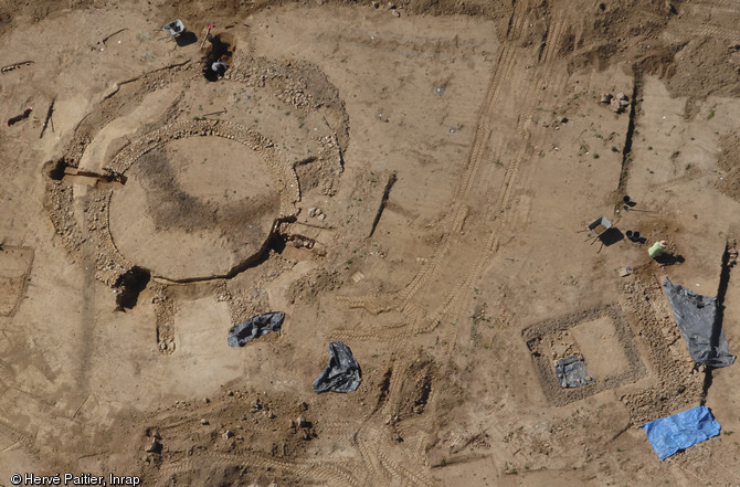 Vue aérienne montrant à gauche trois fana circulaires successifs (12 m de diamètre), et en bas à droite un petit fanum carré (7 m de côté), IIe s. de notre ère, Neuville-sur-Sarthe (Sarthe), 2010.  Par leur forme et leur orientation (leurs entrées sont situées au nord), ces fana circulaires constituent une découverte exceptionnelle en Gaule. Associé à un petit temple rectangulaire, peut-être plus ancien, l'entrée de ce temple était mise en valeur par une pergola de 50 m de long.