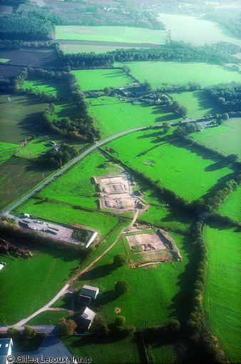 Vue aérienne du chantier d'Allaire (Morbihan) où un segment de la voie antique Vannes-Angers a été mis au jour, 2005.  Au premier plan apparaît le bombement caractéristique de la voie à la surface de la prairie. Au second apparaissent les deux secteurs décapés. Enfin, en arrière-plan, on observe le processus de fossilisation de l'axe antique sous la forme d'un chemin rural et de haies bocagères.     Photo publiée dans le numéro 18 de la revue de l'Inrap <a class= rte-link-ext  href= http://www.inrap.fr/archeologie-preventive/La-Recherche/Archeopages/Numeros-en-ligne/18-19-20-200