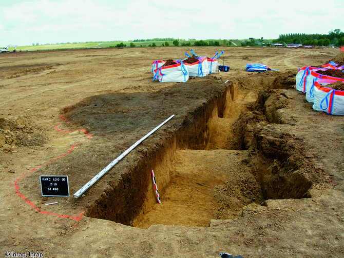 Coupe stratigraphique et mise en sac du remplissage r&eacute;alis&eacute;es &agrave; l'aide d'une mini-pelle, parc logistique de l'Aube, 2006.&nbsp;  A l'image de cette fosse, ce sont plus de 2300 structures, du simple trou de poteau&nbsp;&agrave; la fosse d'extraction de 30m de diam&egrave;tre, qui ont &eacute;t&eacute; test&eacute;es et fouill&eacute;es syst&eacute;matiquement par moiti&eacute;.&nbsp;  &nbsp;  Photo publi&eacute;e dans le num&eacute;ro 20 de la revue de l'Inrap <a class= rte-link-ext  href= http://www.inrap.fr/archeologie-preventive/La-Recherche/Archeopa