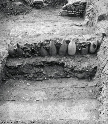 Alignement d'amphores sur le site de la médiathèque à Narbonne (Aude), 2002.  Au cours du second quart du Ier s. avant notre ère, un système de cloisonnement de l'espace au moyen de lignes d'amphores est mis en place, délimitant ainsi des parcelles dont la fonction est encore discutée.  Photo publiée dans le numéro 29 de la revue de l'Inrap <a class= rte-link-ext  href= http://www.inrap.fr/archeologie-preventive/Recherche-scientifique/Archeopages/Les-numeros/28-29-30-HS02-2010/Numero-29/Dossier-Recyclage-et-remploi/p-11771-De-vita-amphorarum.-La-revalorisation-des-amp