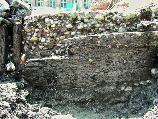 Extrémité est du grand fragment de bordé monté à clin, aménagements portuaires médiévaux de Bordeaux, 2002-2003.  Cette photo illustre la récupération et le réemploi de matériaux dans la construction des aménagements fluviaux de la ville : des galets de lest, des remblais et des pans d'épaves ont été utilisés.  Photo publiée dans le numéro 29 de la revue de l'Inrap <a class= rte-link-ext  href= http://www.inrap.fr/archeologie-preventive/Recherche-scientifique/Archeopages/Les-numeros/28-29-30-HS02-2010/Numero-29/Dossier-Recyclage-et-remploi/p-11774-Le-port-lieu-de-recyclage.-Deux