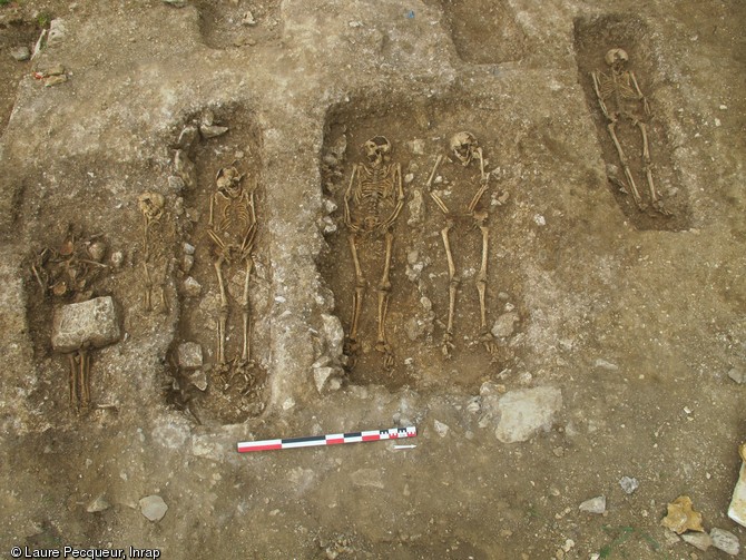 Rangée de cinq sépultures, fin du Ve - début du VIe s., nécropole de Lagny-sur-Marne (Seine-et-Marne), 2010-2011.  Dans la majorité des cas (comme ici), les défunts ont été inhumés sur le dos, la tête orientée vers l'ouest. Les mains sont disposées sur le bassin ou de part et d'autre de celui-ci. Les individus ont été déposés dans un coffrage de bois construit directement sur la fosse, parfois aménagée de pierres. 