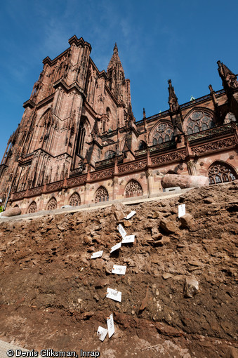 Fouille aux abords de la cath&eacute;drale de Strasbourg (Bas-Rhin), 2012.  &Agrave; l'arri&egrave;re plan la cath&eacute;drale ; au premier plan, les niveaux arch&eacute;ologiques du chantier de construction de cette derni&egrave;re, &eacute;difi&eacute;e entre le XIIe et le XVe s. On retrouve dans ces niveaux quantit&eacute; d'&eacute;clats de gr&egrave;s nous renseignant sur les techniques de taille. 