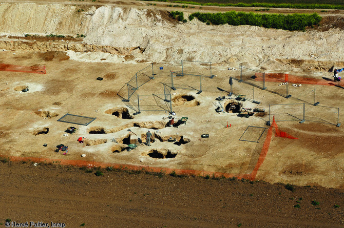 Vue de la partie centrale de la fouille de la minière néolithique de Ri (Orne), 2007.  Près de 650 puits d'extraction du silex, destiné à la fabrication de haches, ont été repérés sur les deux hectares fouillés.  Photo publiée dans le numéro 22 de la revue de l'Inrap <a class= rte-link-ext  href= http://www.inrap.fr/archeologie-preventive/Recherche-scientifique/Archeopages/Les-numeros/HS01-21-22-23-2008/Numero-22/Dossier-Mines-et-carrieres/p-9466-Produire-pour-soi-ou-produire-pour-les-autres.-Role-des-mines-et-carrieres-dans-l-organisation-socio-economique-neolithique.htm  targe