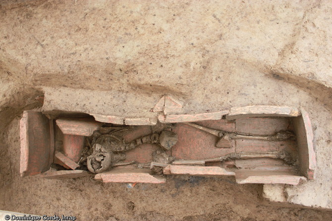 Vue de l'intérieur du coffrage en tuiles de la tombe à libations, Ier-IIIe s. de notre ère, Portbail (Manche), 2012.Une jeune femme y est inhumée avec deux pièces de monnaie en bronze, expression du rite de  l'obole à Charron . Sur la gauche, le coussin céphalique est réalisé au moyen d'une imbrex (tuile arrondie). Le basculement est du à la décomposition du corps.