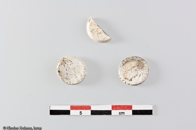 Jetons de jeu en os d&eacute;couverts dans un foss&eacute; de l'enclos n&deg;3, combl&eacute; de r&eacute;sidus de &nbsp;cr&eacute;mation, premi&egrave;re moiti&eacute; du Ier&nbsp;s. de notre &egrave;re, Saint-Marcel (Indre), 2006.Blancs et l&eacute;g&egrave;rement d&eacute;form&eacute;s, ces jetons ont subi une forte chauffe. Ils appartiennent certainement au m&ecirc;me jeu et ont d&ucirc; accompagner le d&eacute;funt sur le b&ucirc;cher fun&eacute;raire.