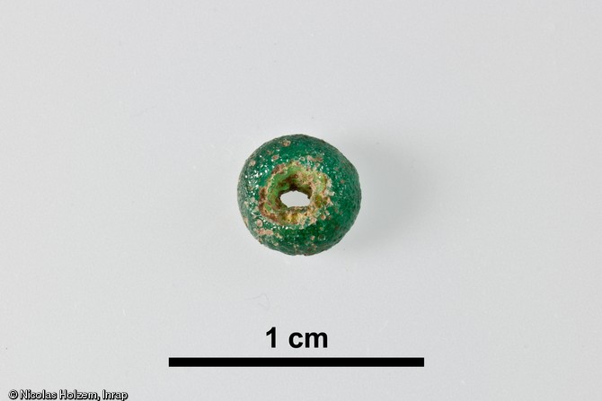 Perle de verre d&eacute;couverte dans un foss&eacute; de l'enclos n&deg;2, combl&eacute; par des r&eacute;sidus de cr&eacute;mation, premi&egrave;re moiti&eacute; du Ier&nbsp;s. de notre &egrave;re, Saint-Marcel (Indre), 2006. Cette perle vert &eacute;meraude, &eacute;l&eacute;ment de parure, a d&ucirc; br&ucirc;ler avec le d&eacute;funt sur le b&ucirc;cher fun&eacute;raire comme en t&eacute;moignent les petites bulles qui ont alt&eacute;r&eacute; sa surface.