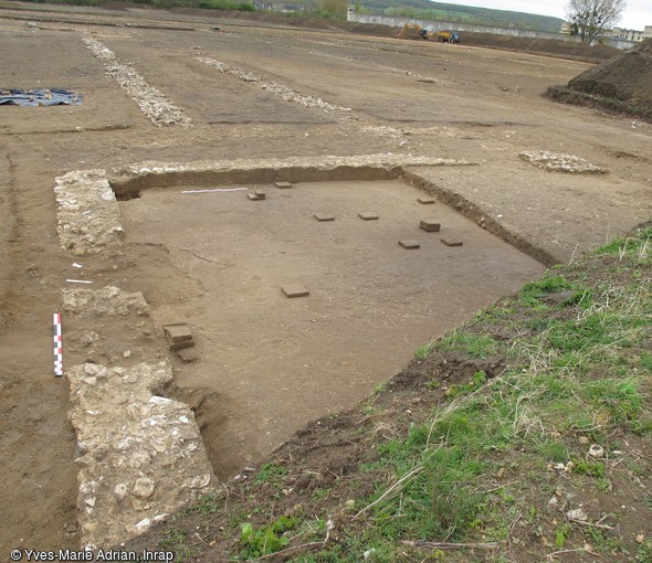 Vue générale d'une pièce chauffée par hypocauste en cours de fouille, Val-de-Reuil (Eure), 2012.À l'arrière-plan se distingue l'une des deux galeries d'un bâtiment résidentiel gallo-romain.